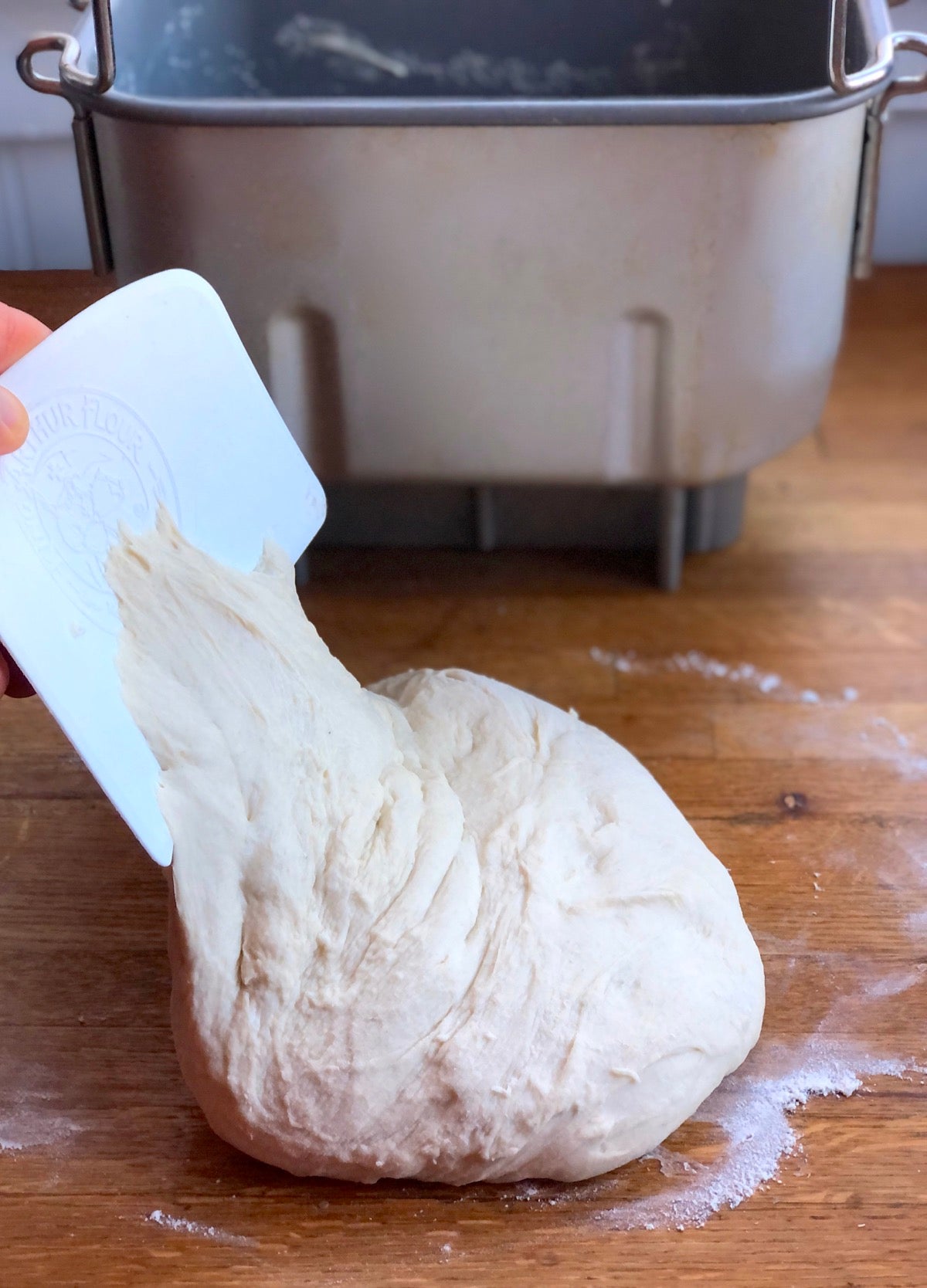 Soft sourdough bread dough on a floured surface being folded with the help of a bowl scraper.