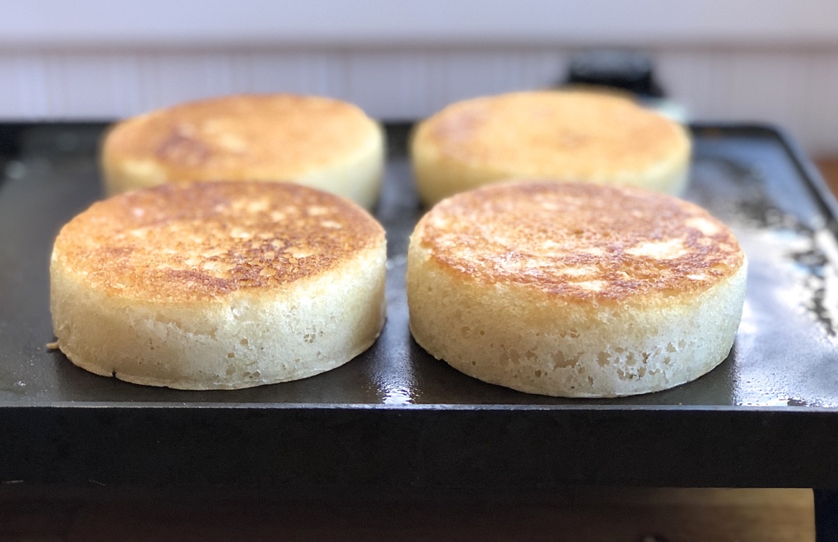 Side view of four sourdough crumpets on a griddle showing their height.