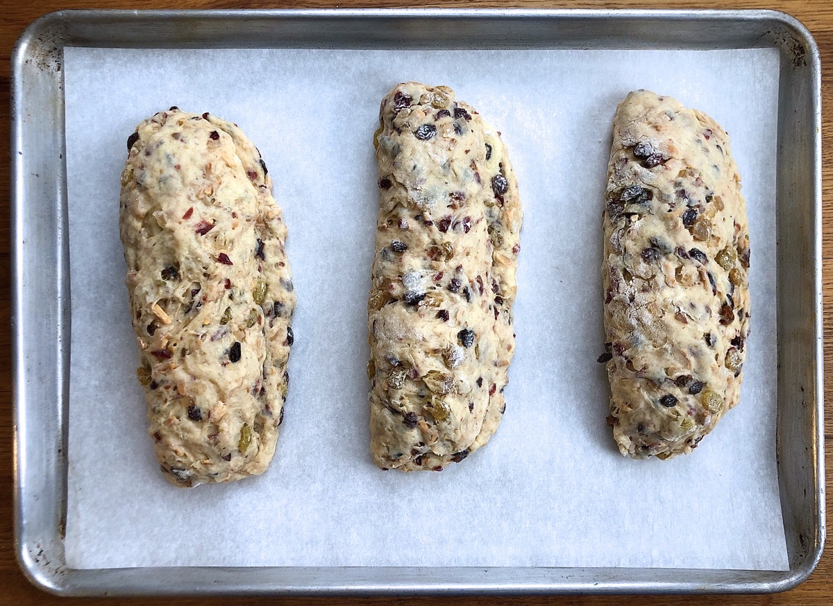 Three stollen positioned on a parchment lined baking sheet, ready to rise.