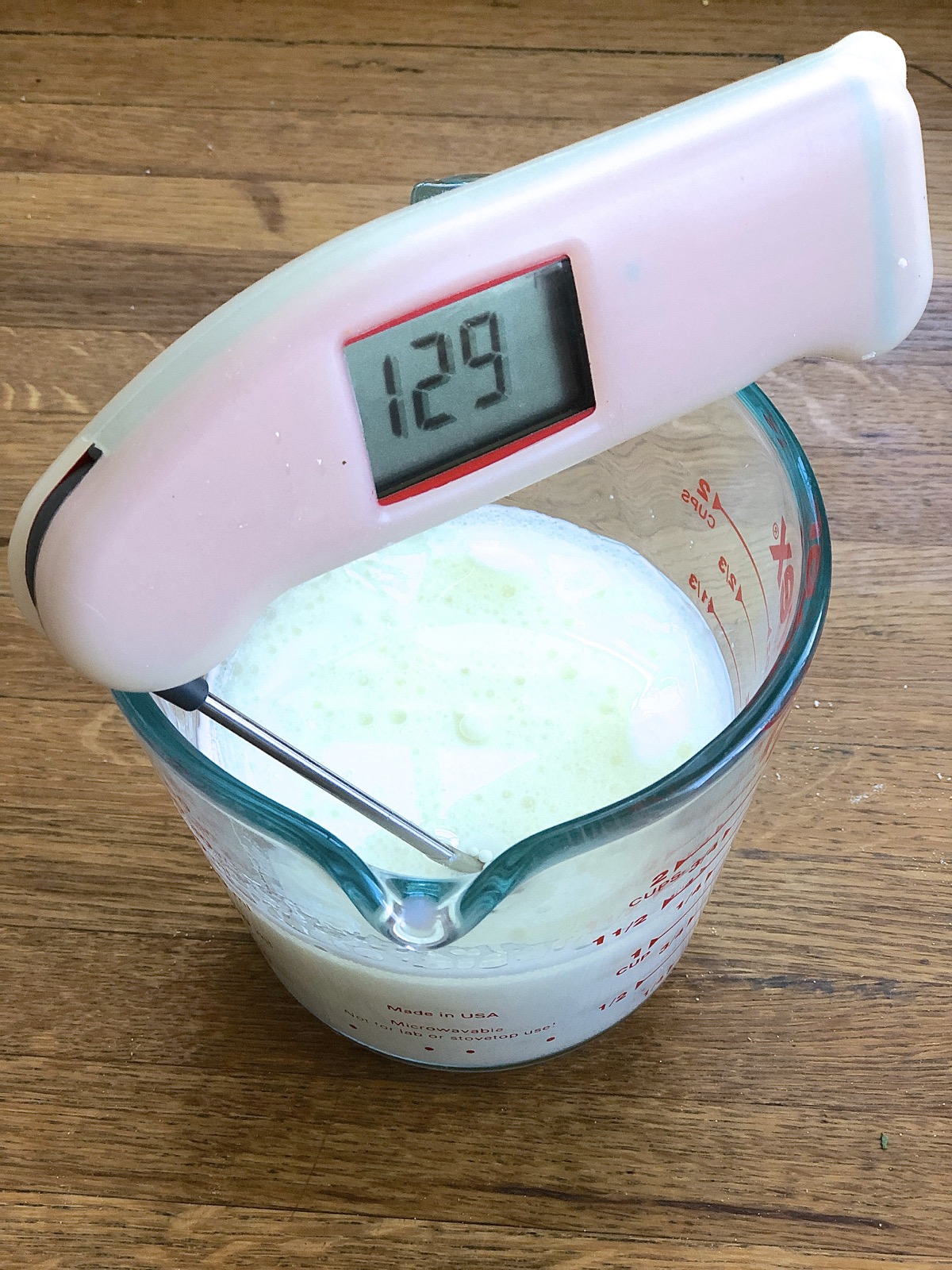 Thermometer in measuring cup of warm milk, showing temperature of 129°F.