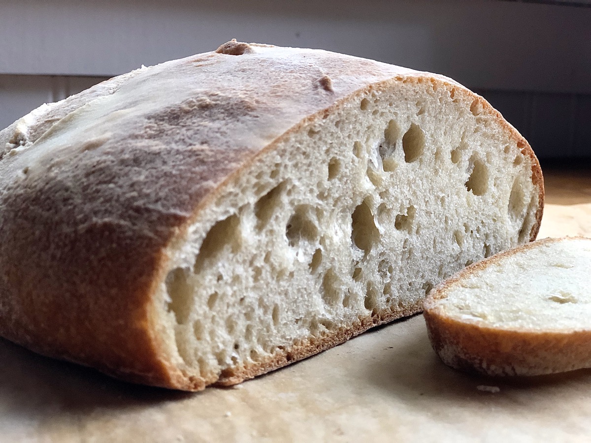 Loaf of bread made with yeast water starter, sliced open to reveal hole-riddled interior.