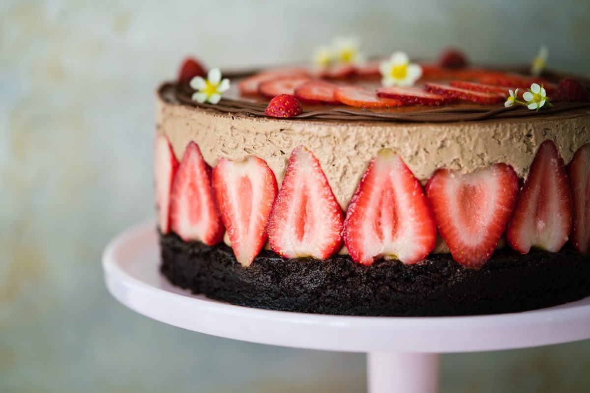 A chocolate and strawberry cream puff cake decorated with strawberries and edible flowers