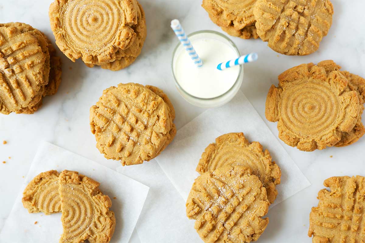 Stacks of peanut butter cookies on a table next to a glass of milk