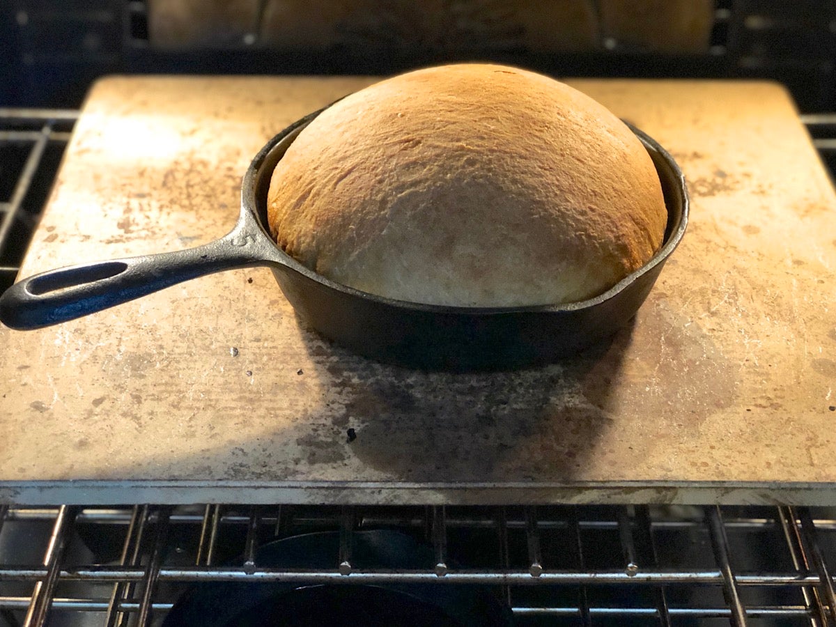 Sourdough bread baking in a cast iron skillet in the oven.