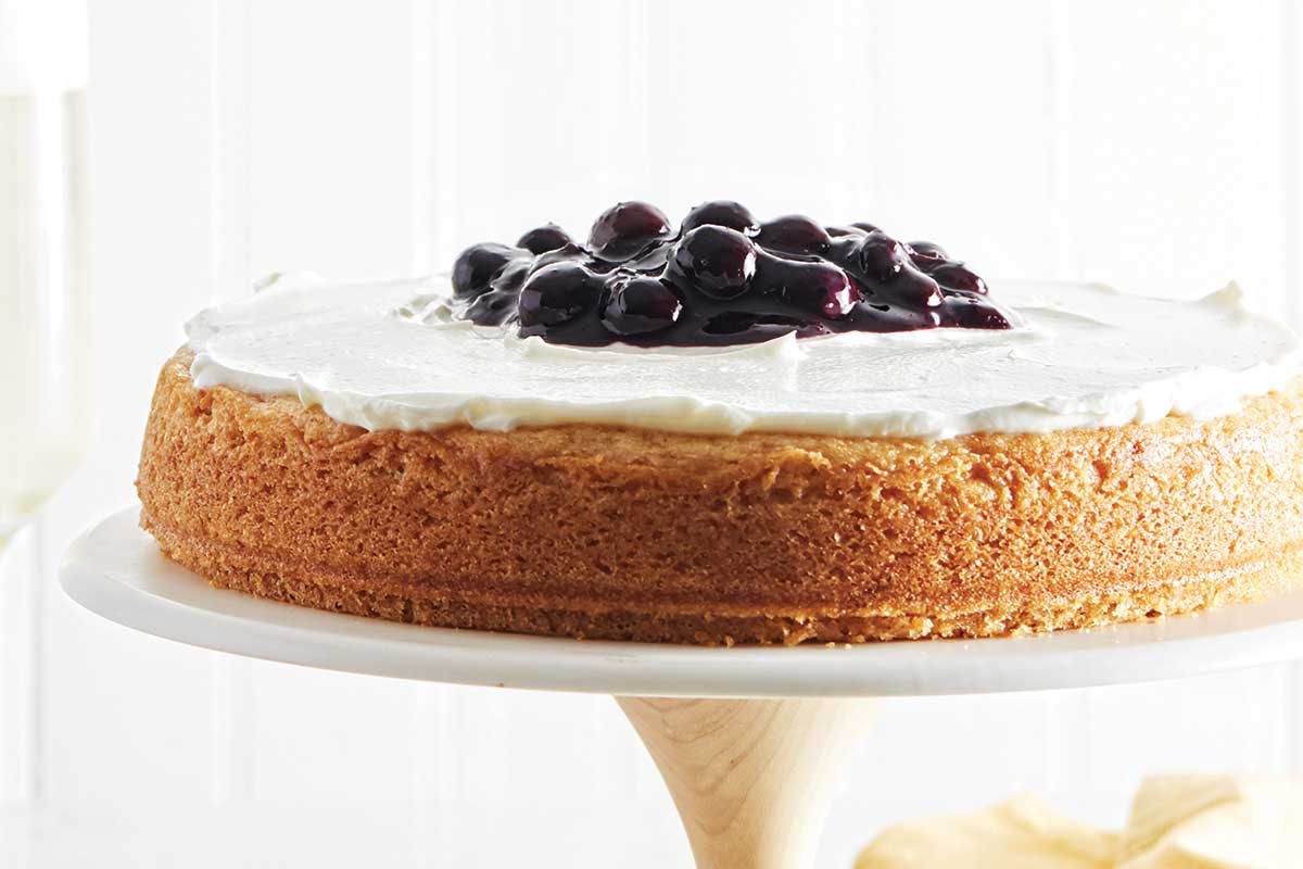 A lemon tendercake topped with blueberry compote on a cake stand