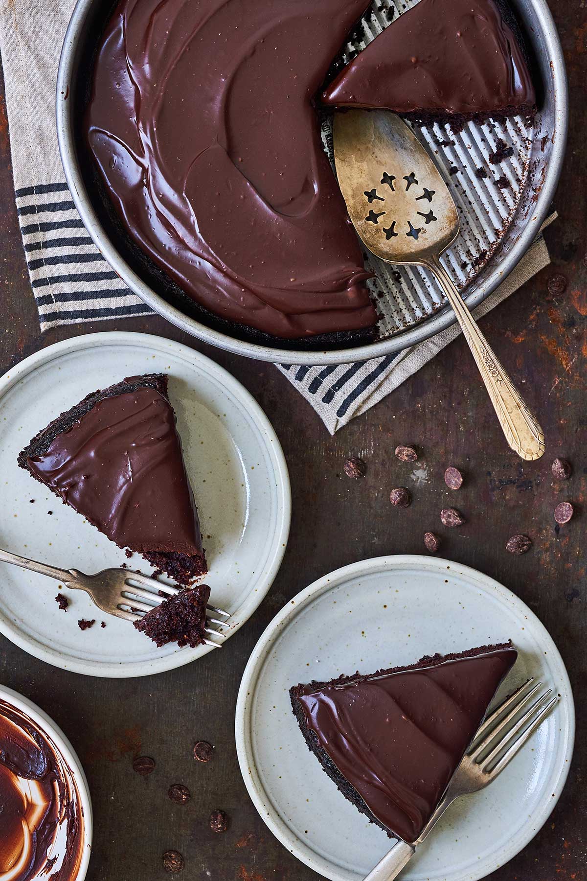 A round chocolate cake topped with chocolate frosting and a few slices on plates