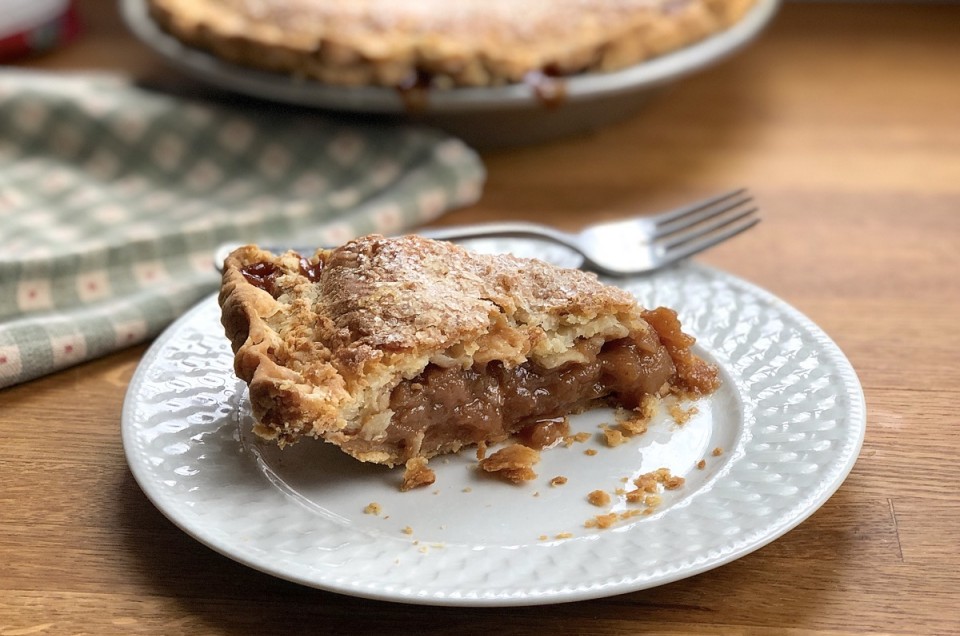 Slice of apple pie on a plate, flakes of crust scattered around slice.