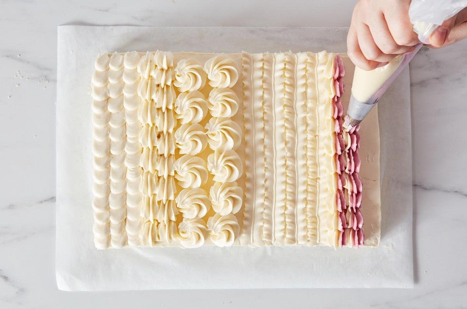 Hands piping designs on a sheet cake