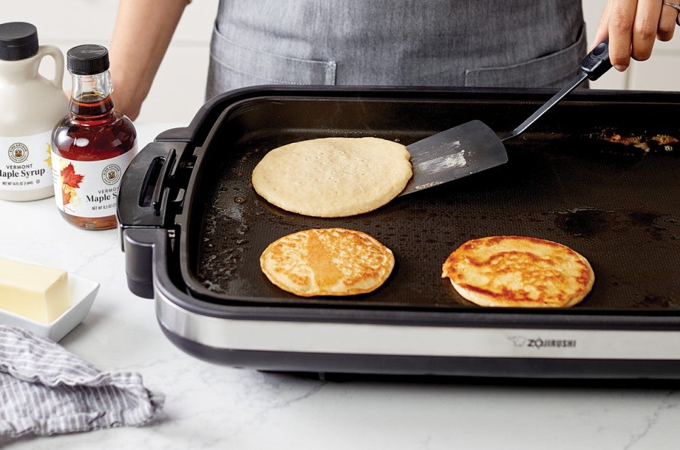 Baker flipping a batch of pancakes on an electric griddle