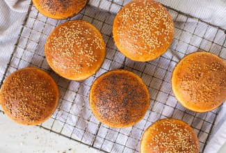 Homemade hamburger buns topped with seeds cooling on a rack