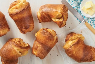 A set of six baked popovers next to a ramekin of butter