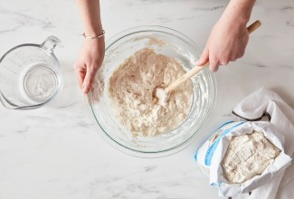 Baker mixing bread dough next to open bag of bread flour