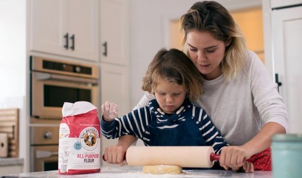 A mother and son using a rolling pin to roll out cookie dough
