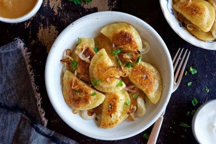 Homemade fried pierogi on a dinner plate, garnished with fried onions and fresh parsley.