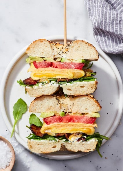 A cross-section showing an Ultimate Sandwich Bagel filled with avocado, tomato, cheese, and greens