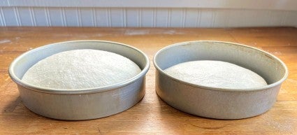 Two round loaves of sourdough bread dough rising side by side, one spiked with commercial yeast for a higher, faster rise.