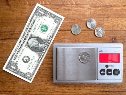 Micro scale with a nickel placed on the weighing platform, dollar bill and more nickels alongside.