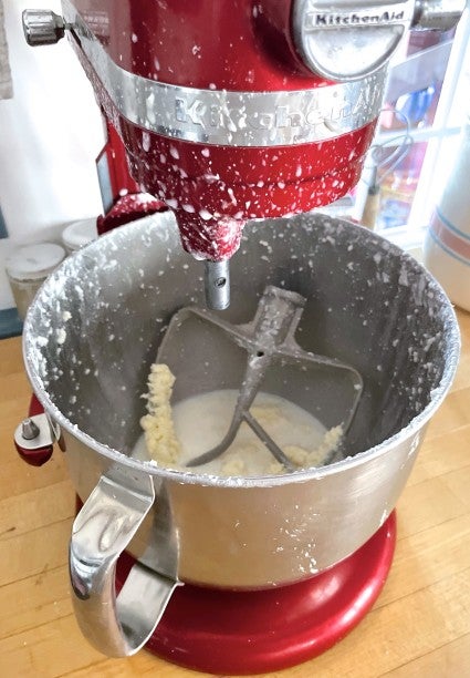 Red KitchenAid stand mixer with bowl of cream, cream shipped on high speed so it splattered all over the mixer and countertop.