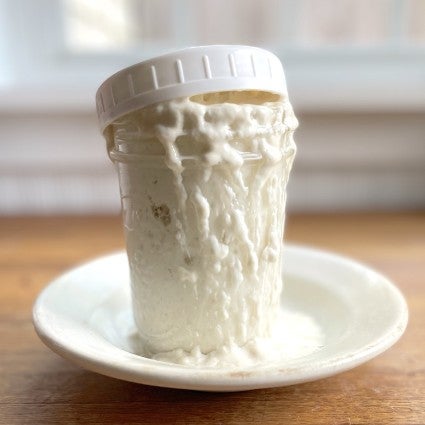 Jar of sourdough starter that's overflowed and run down the sides onto a plate.