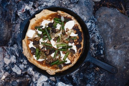 Vegetable pizza being baked in a cast iron skillet over a campfire