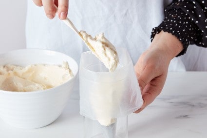 Hands using a glass to set up and fill a pastry bag with frosting