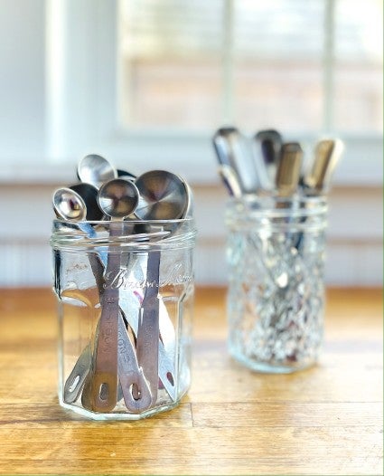 Two sets of measuring spoons, each stashed upright in a glass jar.