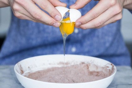 Egg being cracked into bowl full of dry ingredients
