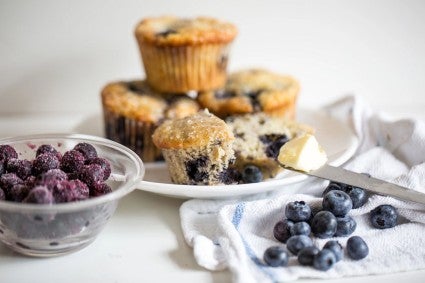 Bowl of frozen blueberries next to blueberry muffins