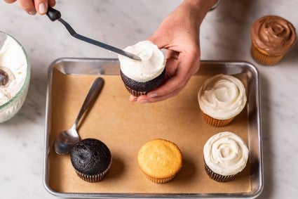 A baker frosting a cupcake with an offset spatula