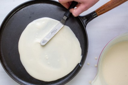 Offset spatula being used to spread thin crepe batter on pan