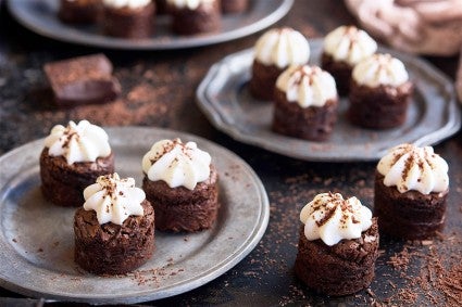 Two platters of mini brownie bites topped with whipped cream and dusted with cinnamon sugar