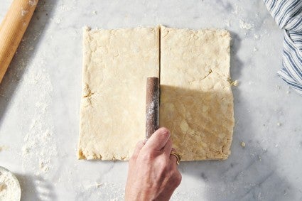 Square of pie dough being cut in half with a bench knife