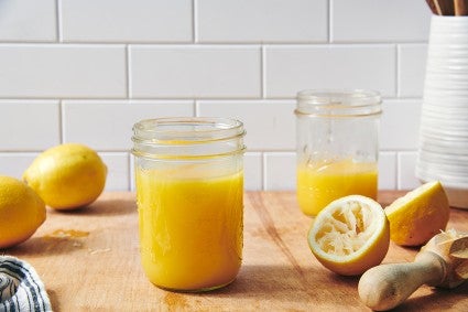 A jar of homemade lemon curd on a table next to squeezed lemons