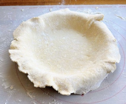 Rolled-out pie crust settled into a pie pan, edges not yet trimmed.
