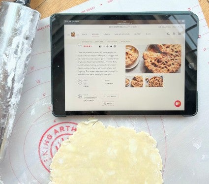 Pie crust rolled on a mat, pictured with a rolling pin and iPad tablet.