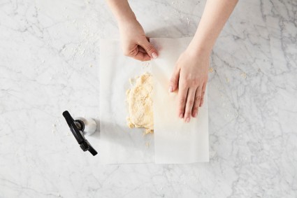 Baker folding pie dough next to a water spray bottle