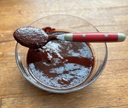 A bowl of oily, grainy ganache with a spoon of ganache resting on the rim of the bowl..