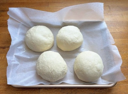 Four balls of just-shaped pizza dough on a baking sheet ready to go into the freezer.