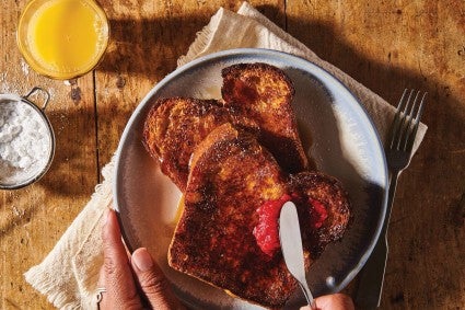 Two slices of French toast on a plate; a baker spreads berry jam on top