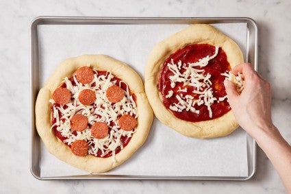 Parbaked pizza dough being topped with sauce, cheese, and pepperoni