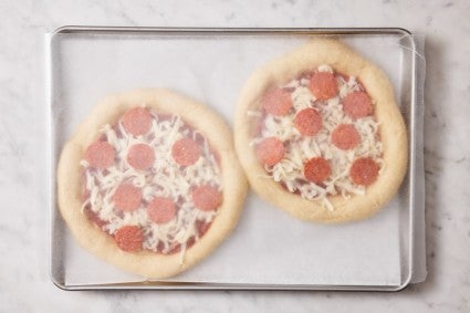 Parbaked and topped pizzas on a baking sheet and covered with a piece of wax paper